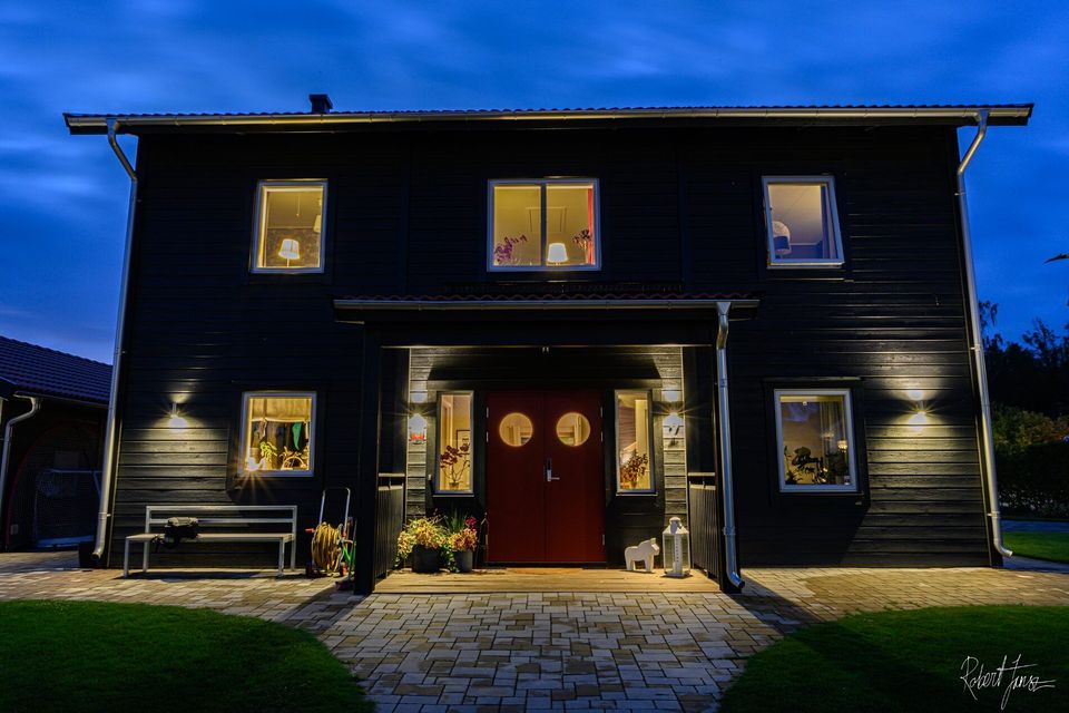 Svart trähus med tända fönster i skymningen