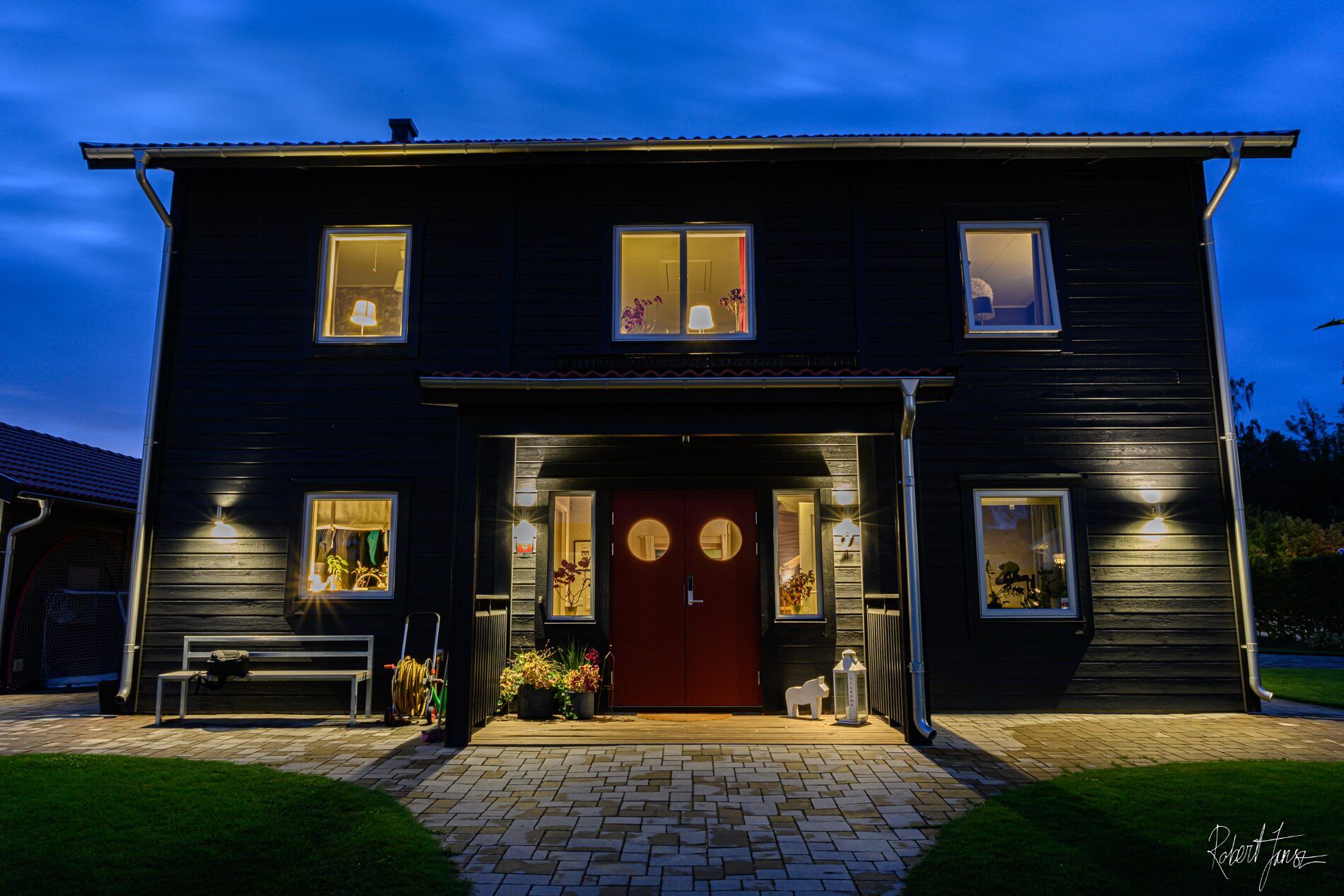 Svart trähus med tända fönster i skymningen